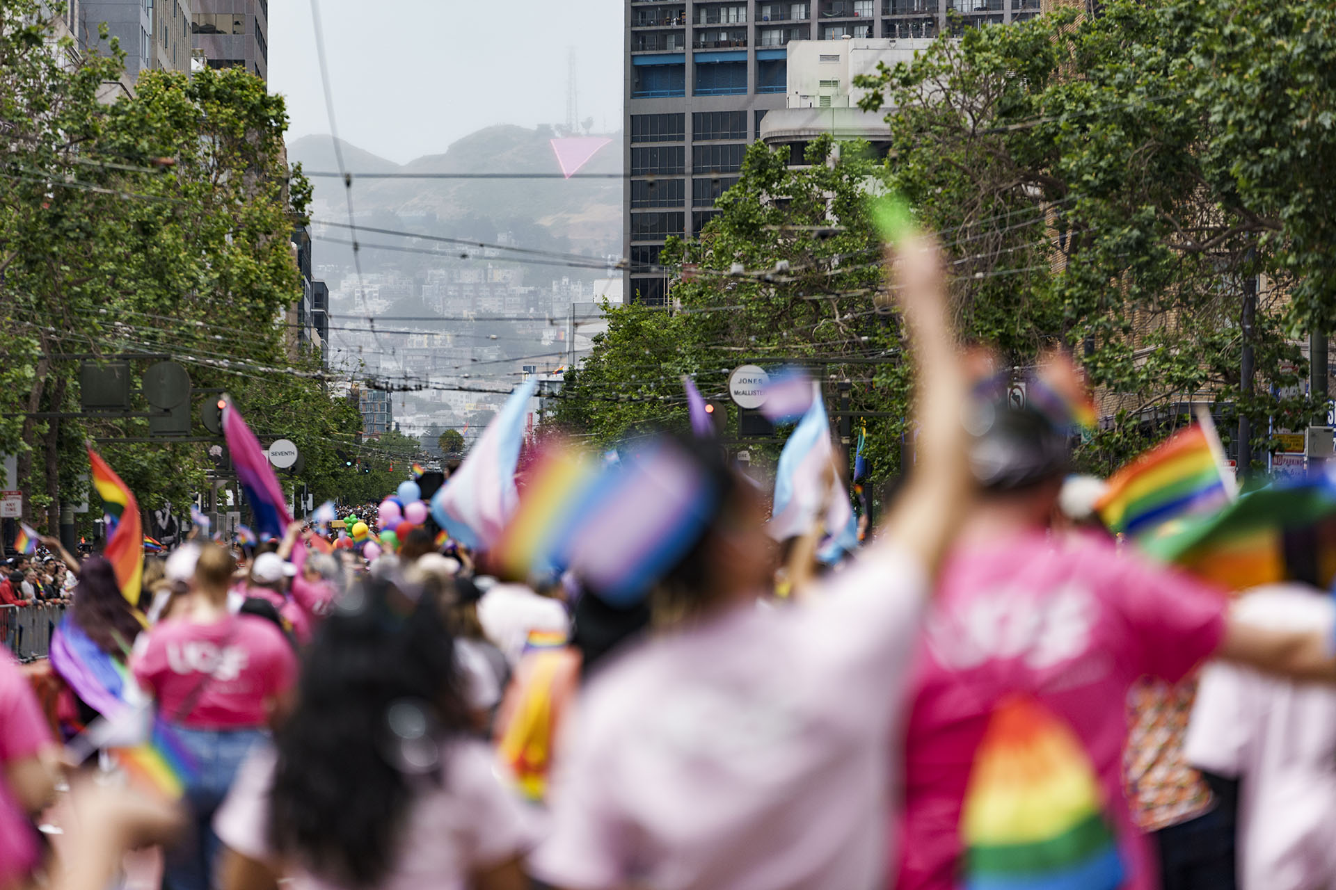UCSF community members participate in the 2024 San Francisco Pride parade with large-scale pink triangle art installation appearing through buildings framing the hillside of Twin Peaks in the distance.